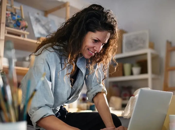 A woman smiles while working on her laptop, showcasing a moment of joy and productivity.