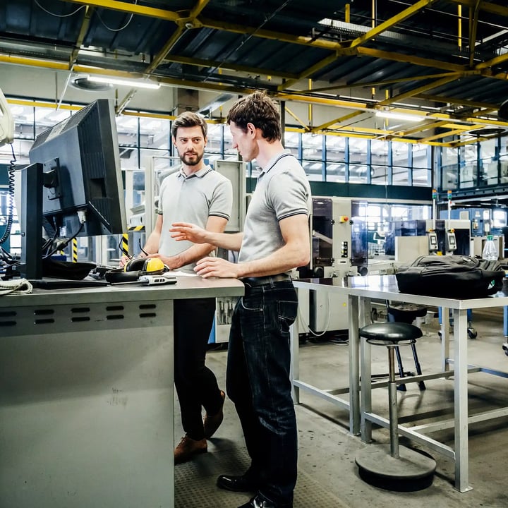 Two men in a factory examining a computer screen, engaged in a discussion about production processes.