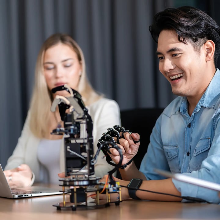 A women and a man sitting together testing a robotic arm.