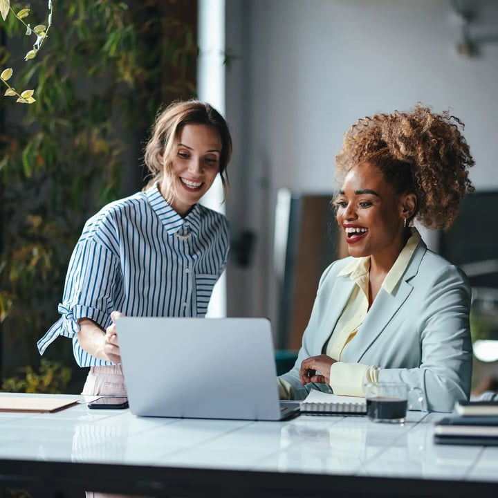 Two business women smiling and laughing looking at computer screen together.