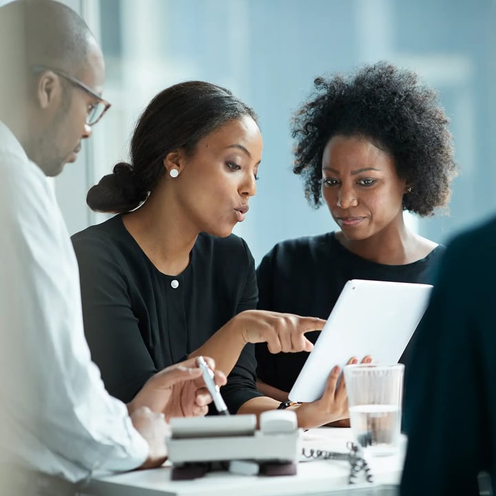 Two women entrepreneurs collaborate at a table, focused on their tablet as they share ideas.