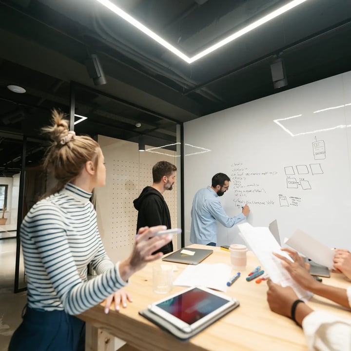 Two men entrepreneurs brainstorm in an office, one sketching ideas on a whiteboard while the other attentively observes.