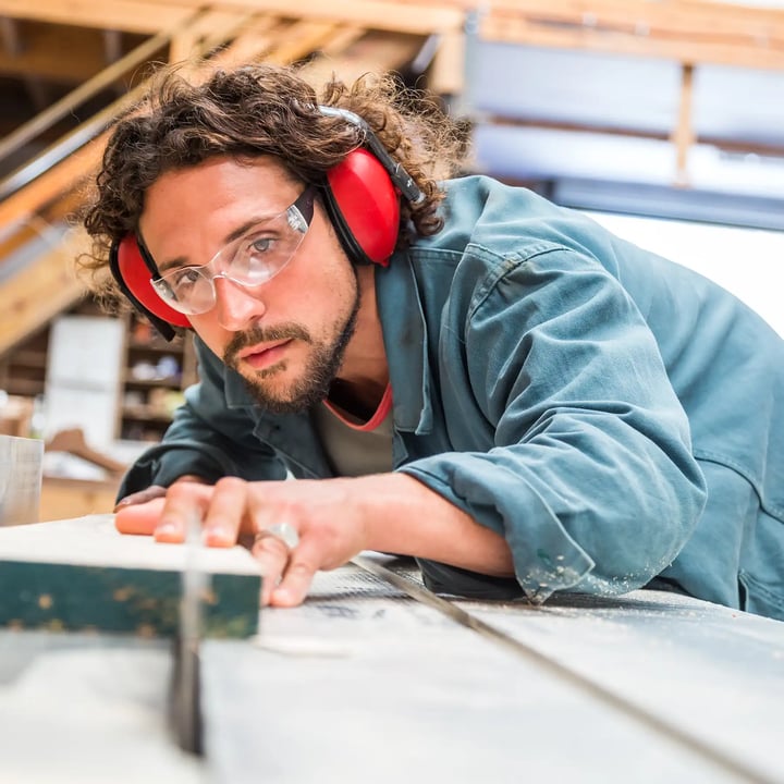 Un homme portant des protections auditives et des écouteurs se concentre sur son travail sur une table en bois, garantissant sécurité et concentration.