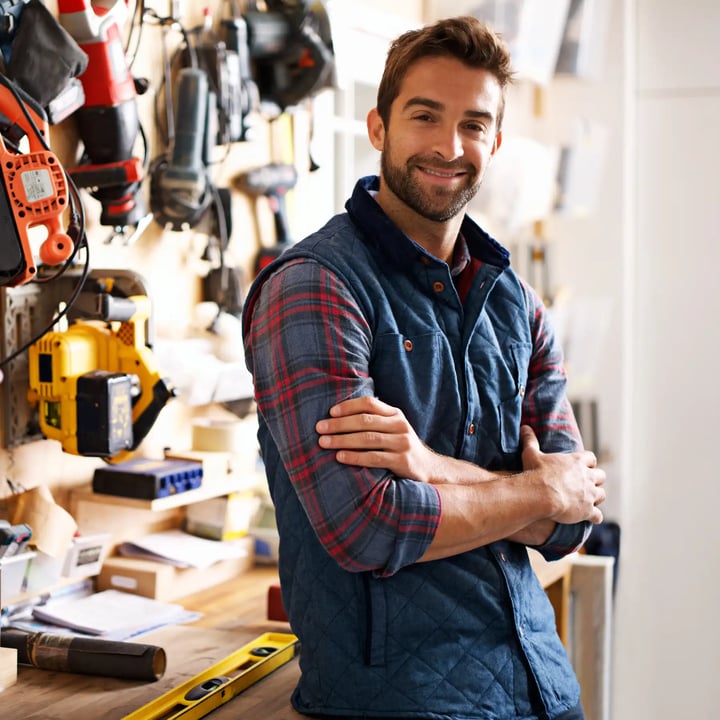 Un homme pose devant un mur rempli de divers outils, mettant en valeur un espace de travail bien organisé.