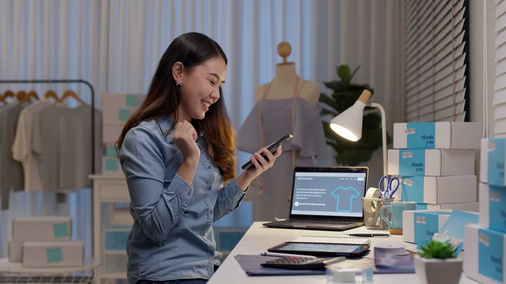 Une femme assise à un bureau, concentrée sur son téléphone, entourée d’un espace de travail bien rangé et d’un éclairage tamisé.