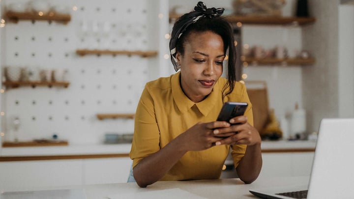 Une femme vêtue d’une chemise jaune regarde attentivement son téléphone, absorbée par son écran.