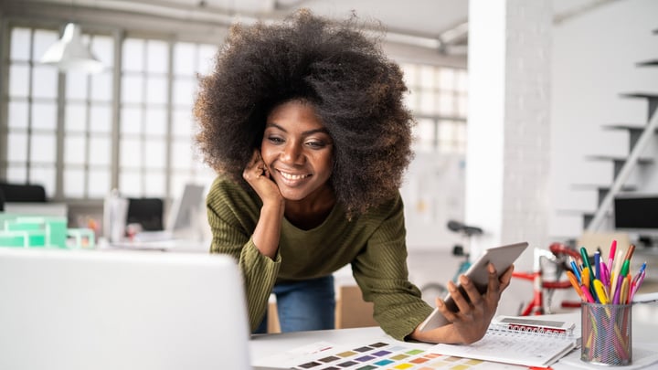 A woman with afro hair focused on her laptop, engaged in work in a bright and modern workspace.