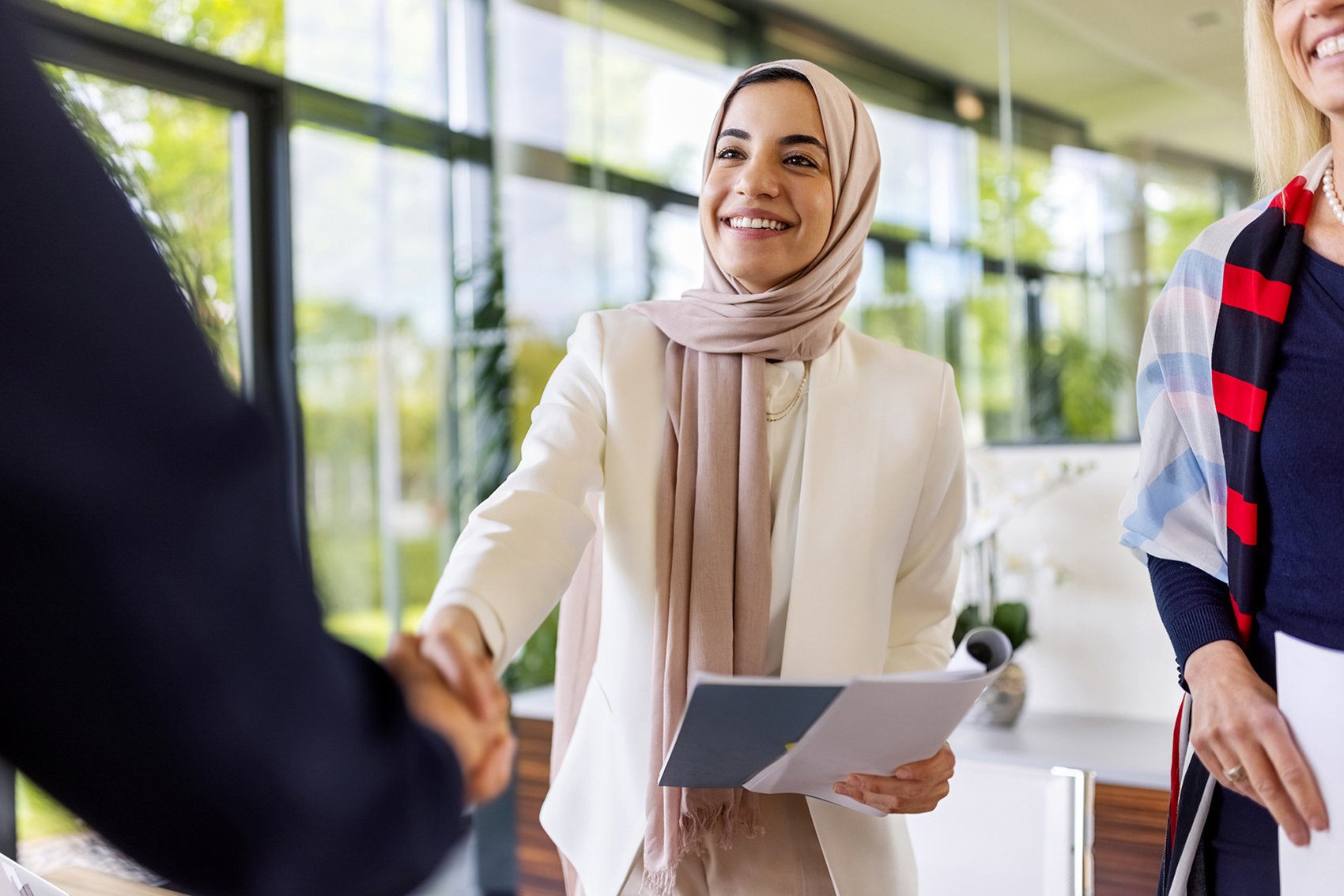 A smiling woman shakes hands with another professional.