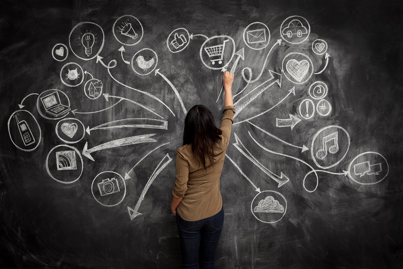 A woman writing on a chalkboard with various symbols and icons.