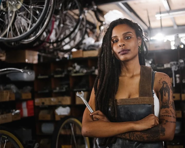 A woman with dreadlocks stands confidently in a vibrant bike shop, surrounded by various bicycles and accessories.