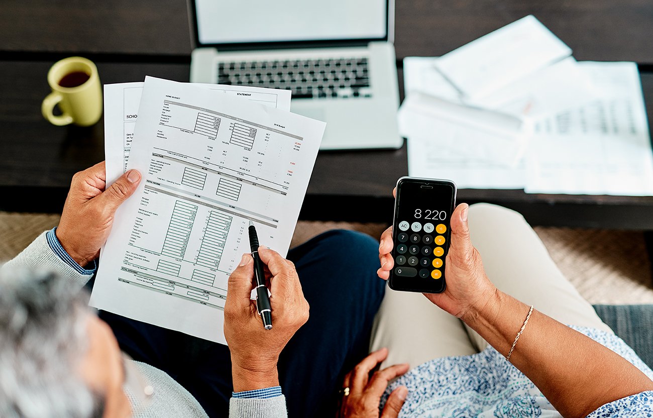 An elderly man and woman discuss finances using a spreadsheet and an iPhone calculator.