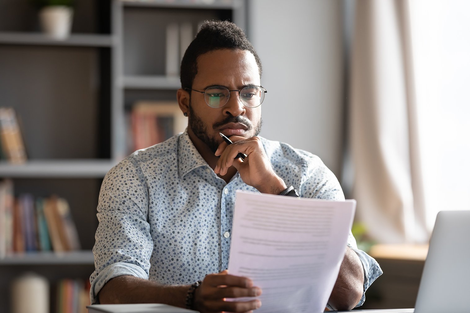 Un homme portant des lunettes se concentre sur un document qu'il tient.
