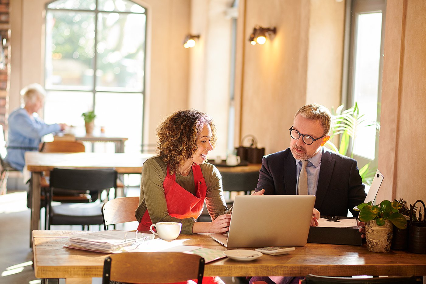 A business woman and a business man discuss the contents of a laptop while sitting in a cafe. 