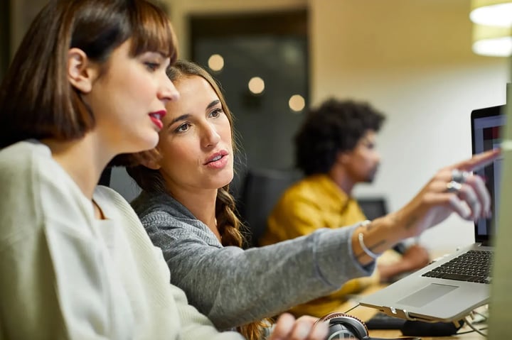 Two women collaborating on a computer, focused on their work and sharing ideas in a professional environment.