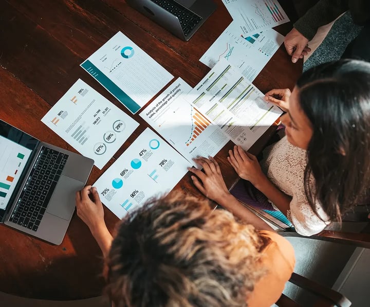A group of individuals collaborating on a laptop surrounded by papers and graphs, focused on their work.