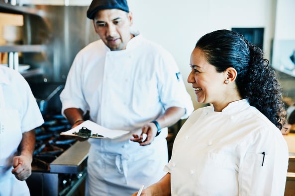 Three chefs discuss work duties in a restaurant kitchen.