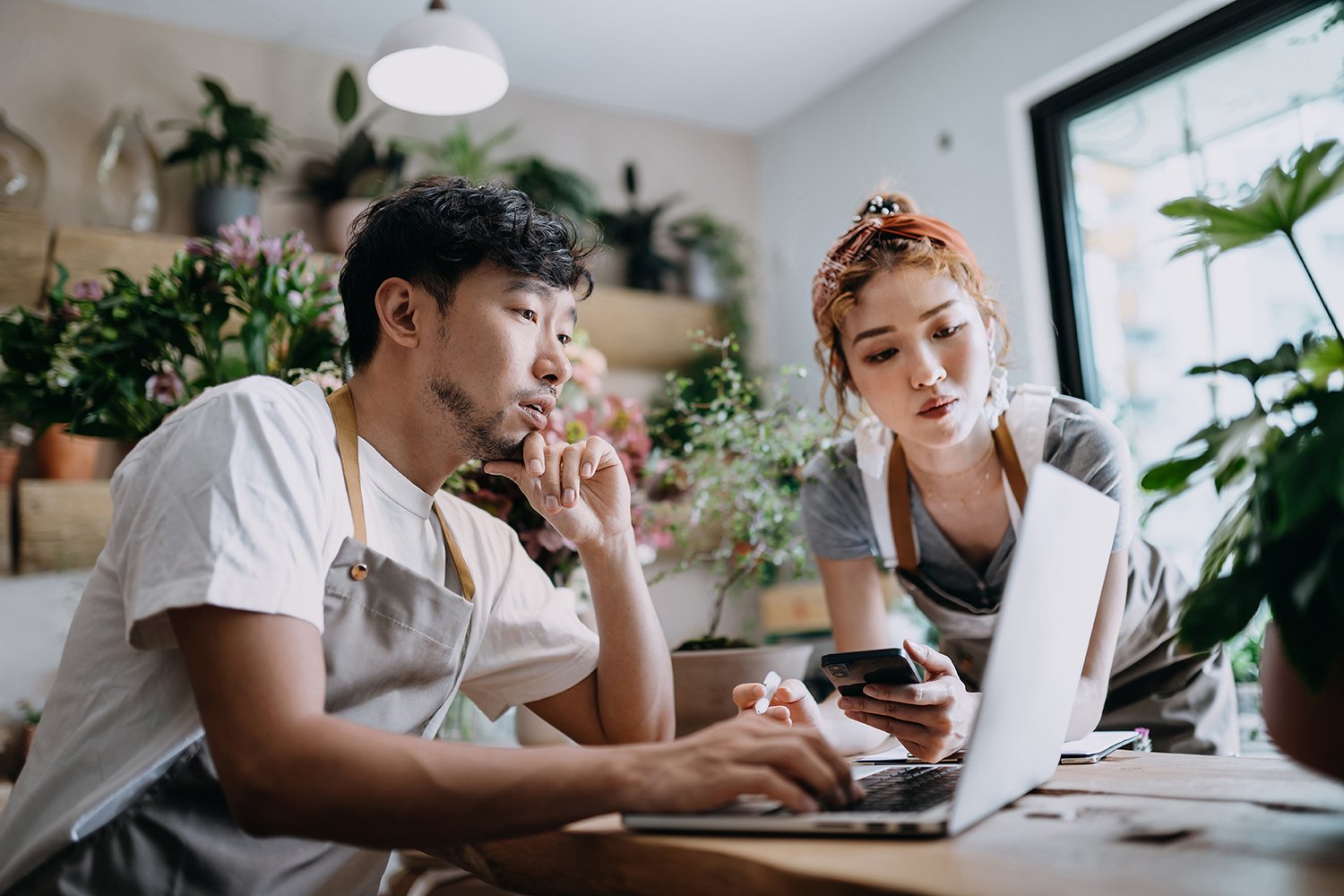 A male employee and female employee look at a laptop in a floral shop.