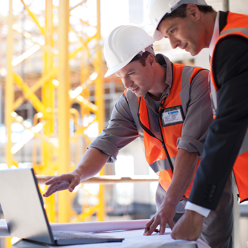 Two male construction workers looking at a laptop.