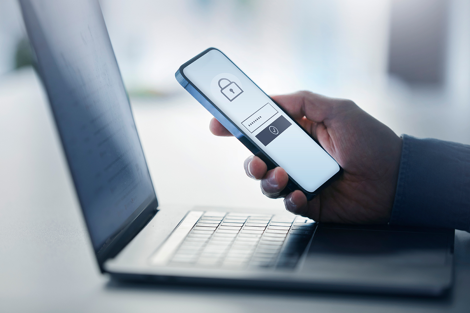 A hand holding a cellphone in front of a laptop