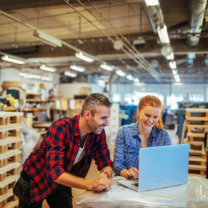 A man in red and a woman in blue work together at a laptop.