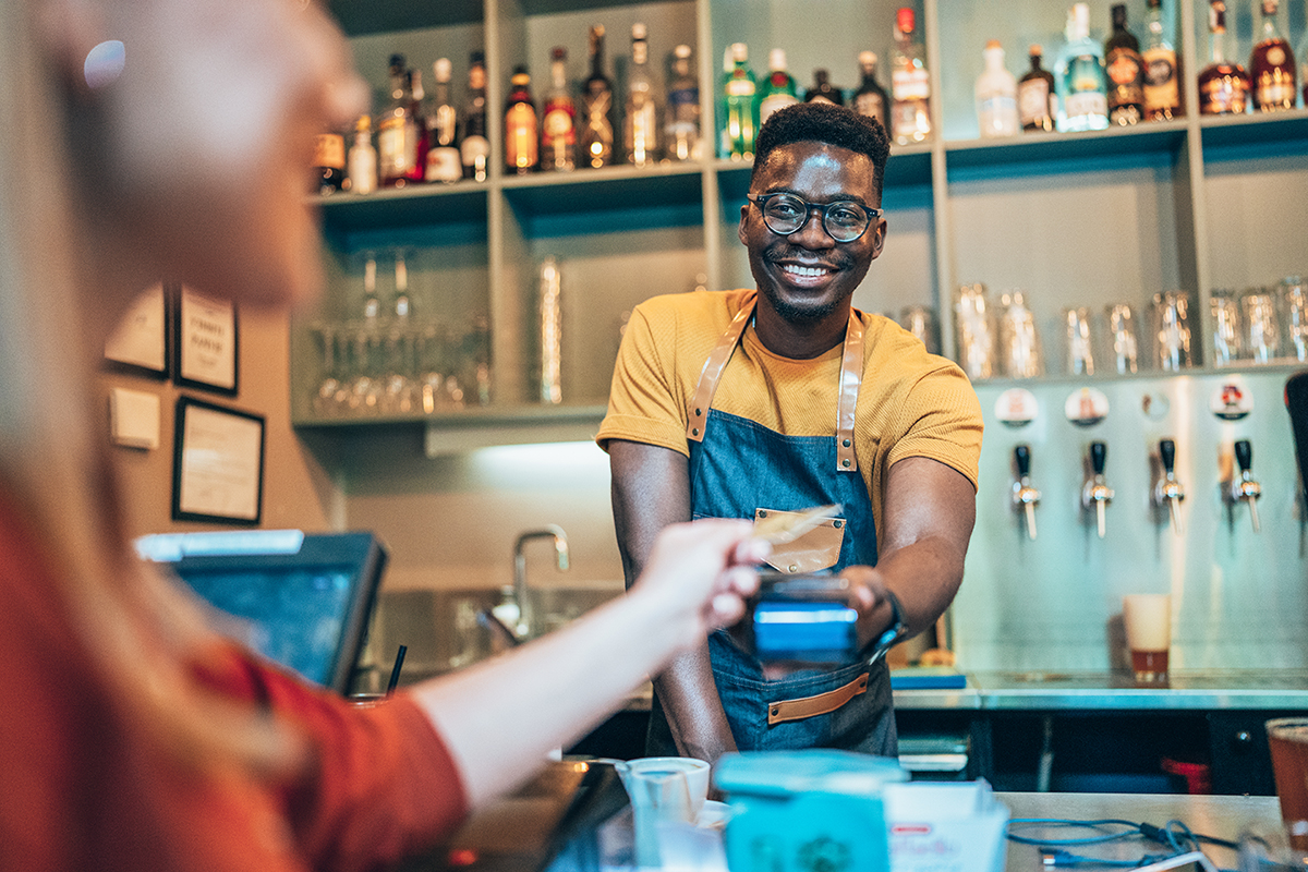 Un employé de café, debout derrière un comptoir, souriant et acceptant un paiement par carte de crédit.