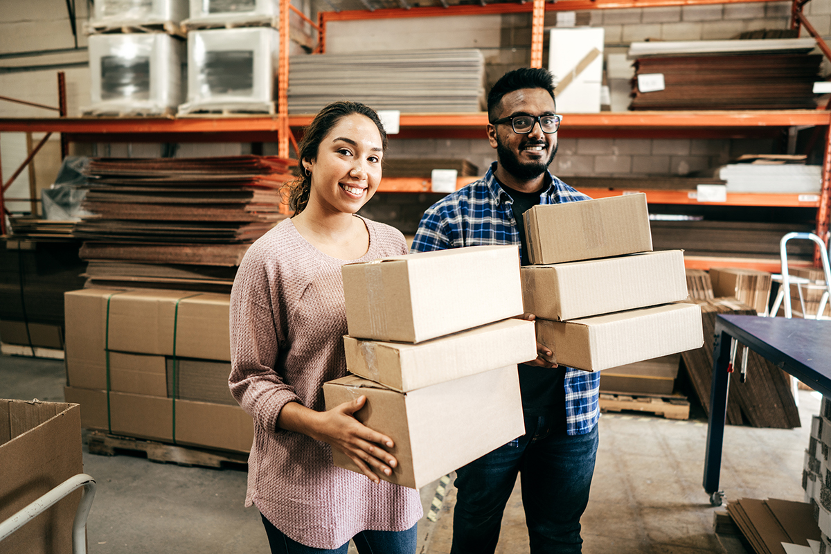 Deux employés souriants tiennent des boîtes dans un entrepôt.